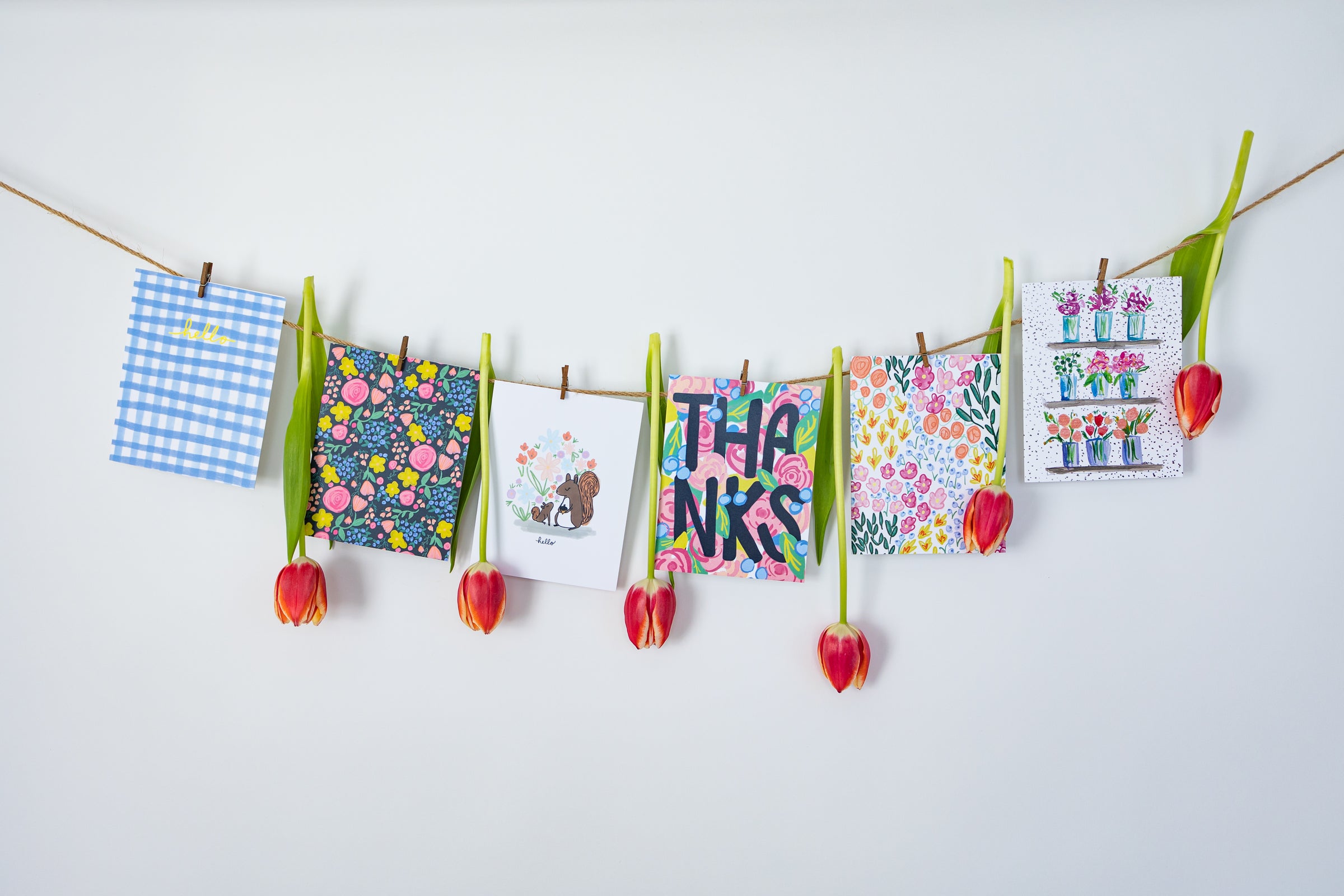 A visually captivating image showcases a vibrant collection of greeting cards gracefully suspended on a line of twine. The colorful cards, each uniquely designed, sway gently in the breeze, adding a playful and cheerful atmosphere. 